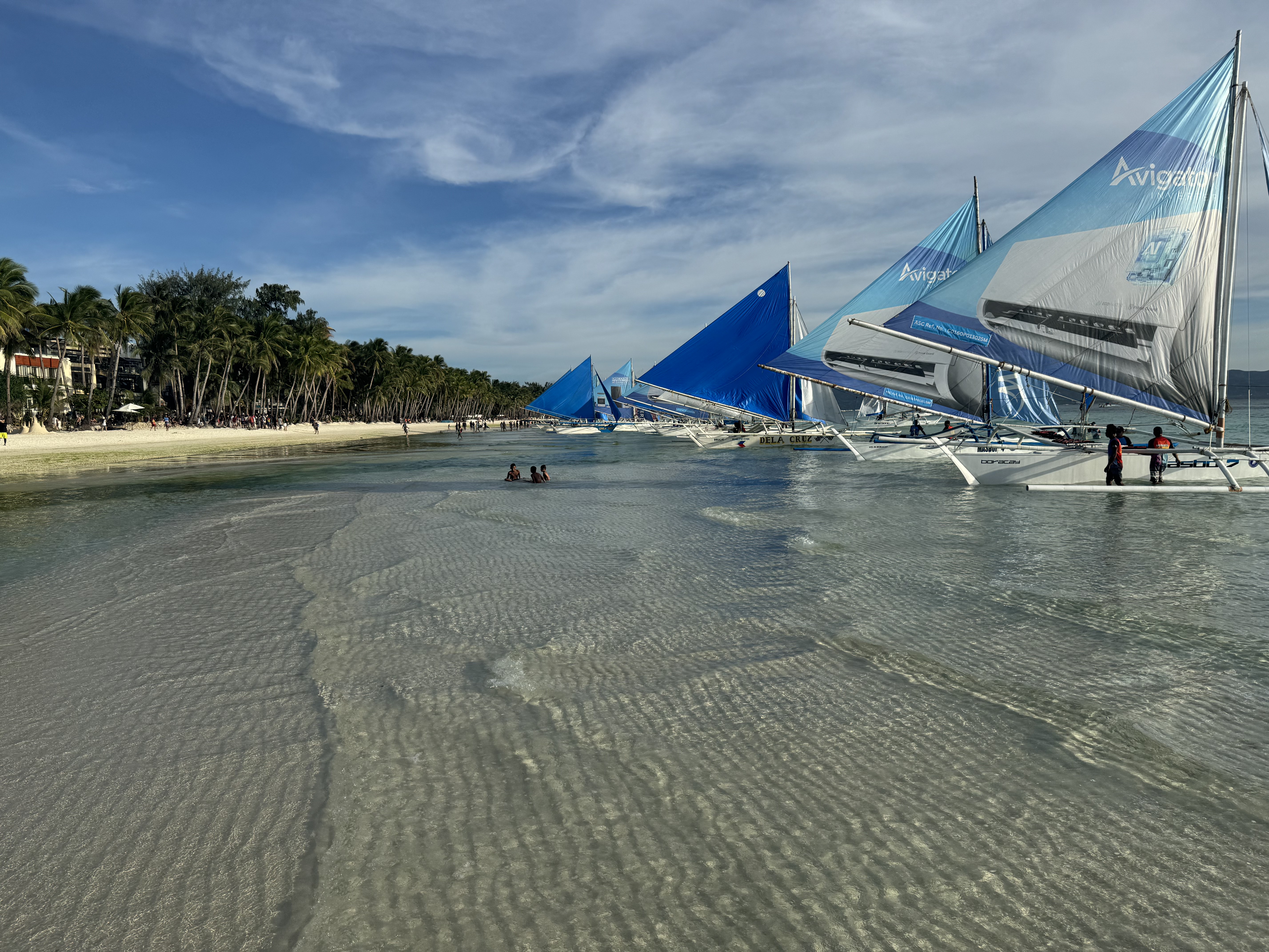 Traditional paraw sailboats gliding through shallow turquoise water.